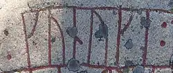 Das Foto zeigt einen Ausschnitt eines hellgrauen Steins mit einer rot nachgezogenen Runeninschrift darauf.