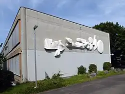 Kalligraphie. Entwurf zum Relief aus Marmor 1975 von Helene Balmer. Ausführung von Lorenz Balmer, 1982. (Breite 12,5 Meter). Sekundarschule II Fröschmatt, Pratteln
