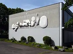 Kalligraphie. Entwurf zum Relief aus Marmor 1975 von Helene Balmer. Ausführung von Lorenz Balmer, 1982. (Breite 12,5 Meter). Sekundarschule II Fröschmatt, Pratteln