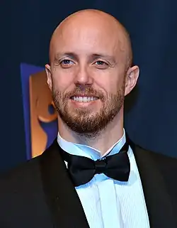 Lars Frölander im Anzug mit schwarzer Fliege trägt eine Glatze und einen Bart.