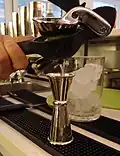 Limettensaft wird mit einer Limettenzange in einen japanischen Jigger gepresst