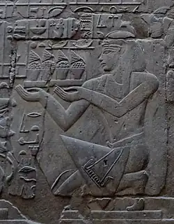 Relief eines kunstvoll gekleideten Mannes, der kniend ein Tablett mit Speisen und Blumen hält