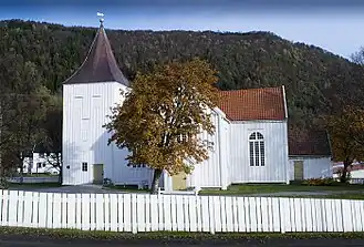 Foto einer weißen Holzkirche, im Hintergrund eine Erhebung