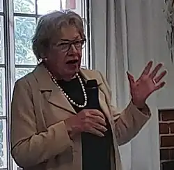Margaret Reid 2021. Eine ältere Frau mit einer schweren Perlenkette gestikuliert beim Reden.