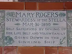A tablet formed of two large tiles, bordered by green flowers in the style of the Arts and Crafts movement