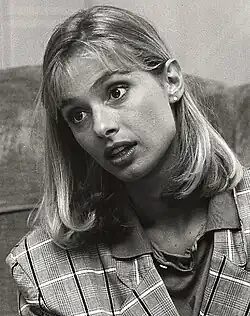 Schwarz-weiß Porträt aus dem Jahre 1987 von Maryam d’Abo mit blonden, schulterlangen Haaren, die einen interessierten Gesichtsausdruck zeigt. Sie trägt ein kariertes Jackett und ein Hemd mit Kragen trägt. Im Hintergrund scheint eine strukturierte Oberfläche zu sein, möglicherweise eine Wand oder ein Möbelstück.