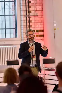 Matthias Kettemann in einem Raum stehend mit einem Mikrofon in der Hand.