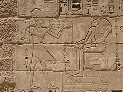 Relief eines Mannes mit Krone, der ein Tablett mit Speisen vor einem sitzenden Mann mit Widderkopf hält