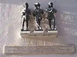 Figurengruppe auf der Nordseite des Karlstores in München („Die drei Musikanten“), von Konrad Knoll. Die Gruppe war Bestandteil des alten Fischbrunnen der von 1884 bis 1944 am Marienplatz stand.