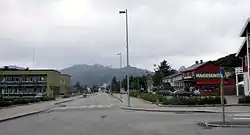 Foto einer Straße, links und rechts davon Gebäude, im Hintergrund Berge