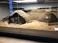 Hinter einer Glaswand ist eine Miniatur von hügelförmigen Häusern zu sehen.