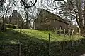 Eine einfache Kapelle hinter Bäumen; auf der linken Seite befinden sich Ruinen eines Schlosse