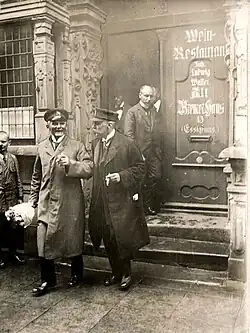 Schwarz-weiß-Fotografie von mehrere Personen, die aus einer Tür ein Gebäude verlassen. An der Tür steht „Wein-Restaurant“