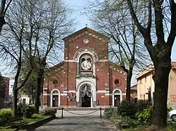 Kirchengebäude in moderner Bauweise aus roten Backsteinen zentral vorn vorn mit Zuwegung und Vorplatz.
