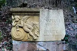 Wegweiser zur Lorettokapelle Murbach mit der Spolie «Genius auf einer Schnecke»