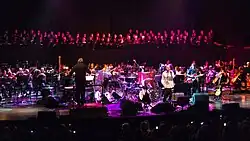 Darstellung der verschiedenen Ensemble und mitwirkenden Musiker von vorne aus dem Konzertsaal in Farbe.