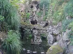 Ein See mit Wasserfall und dahinterliegendem Höhlensystem.