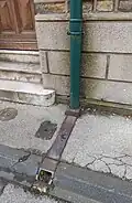 Fallrohr mit Bodenanschluss an eine Gehwegrinne, die in die Gosse entwässert