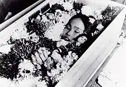 Schwarz-Weiß-Aufnahme des mit Blumen geschmückten Sargs von Sadako Sasaki. Nur das Gesicht des Kindes ist nicht von Blumen bedeckt.