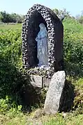 Antiker Kreuzstein mit Swastika neben einer modernen Ädikula-Heiligenfigur an der St.-Brigid-Quelle bei Cliffoney, County Sligo (Irland)