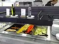 Kleine Salatbar in einem Schnellrestaurant, hier mit Glasplatten als Ablagen und Hustenschutz.