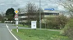 links Straße, in der Mitte umgeben von Bäumen ein Werksgebäude der Sandler AG