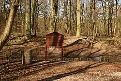 Schautafel und Gedenkstein, im Hintergrund Graben und Wälle der Schlossruine