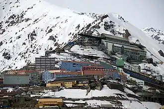 Oben die Schienenrampe, wo die Erze aus dem Teniente-5-Stollen kommend in die Erzmühle gekippt werden. In der unteren Hälfte Teile der historischen Bergbaustadt Sewell. Etwa 3&nbsp;km hinter dieser Anlage befindet sich der Berg, in dem das Erz abgebaut wird.