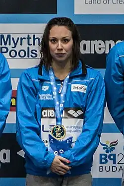 Silvia Di Pietro mit grauer Trainingshose und hellblauer Trainingsjacke steht vor einer Werbewand mit Aufschriften in lateinischer Schrift.