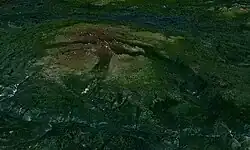 Bewachsenes Gelände mit einem felsigen Berg mit sanften Hängen, in die weite Täler eingeschnitten sind, der sich über die Landschaft erhebt
