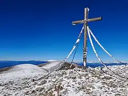 Von Raureif überzogenes Gipfelkreuz des Speikkogels, im Hintergrund der Lenzmoarkogel