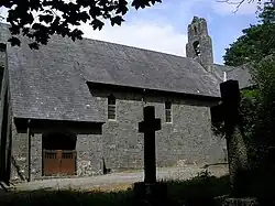 Teil einer steinernen Kirche mit hohem Schieferdach; links befindet sich eine leicht vorspringende Veranda mit hölzernen Türen, auf dem First befindet sich ein Glockenstuhl