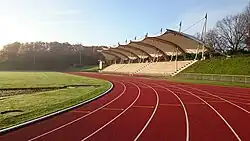 Foto des Stadions Gladbeck mit überdachter Tribüne, Laufbahn und Rasenfläche in der Morgensonne