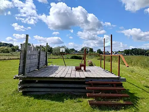 Das Segment mit Palisadenfront (links) und begehbarer Oberfläche. In der Mitte ein Podest für Besucher. Wenn Besucher durch die Tafel (rechts oben) blicken, wird ihnen die Lage des Sperrwerks in der heutigen Landschaft angezeigt.