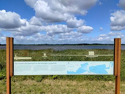 Visualisierung „Das historische Sperrwerk in der heutigen Landschaft“ am Sperrwerk-Modell. Der Fotograf hat die Kamera allerdings zu hoch gehalten. Vom richtigen Blickpunkt aus erscheinen das Sperrwerk und die Schiffe im Wasser der Schlei.