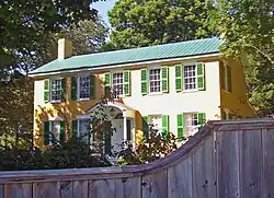 Ein gelbes Haus mit grünen Fensterläden und einem Holzzaun im Vordergrund