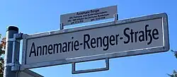 Foto eines weißen Straßenschildes mit schwarzer Schrift "Annemarie-Renger-Straße", das an einem Metallpfahl befestigt ist