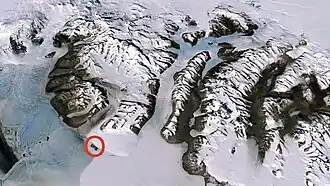 Die eisfreien The Strand Moraines (roter Kreis) an der Westflanke der Mündung des Koettlitz-Gletschers (links) auf halber Strecke zur schneebedeckten Landspitze des Butter Point (Mitte links)