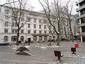 Pflasterwellen mit Wasserspiel, Platanen, Stühle am Nordende. Rechts die Hamburgische Landesbank (heute Hamburg Commercial Bank). Hinten über die gesamte Breite das Thalia Theater.
