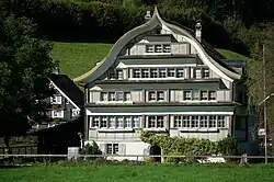 Fabrikanten- und Handelshaus mit Schweifgiebeldach aus dem Jahr 1813, Eingang mit Rundbogenportal und über Ost- und Westseite durch­laufendem Klebdach in Spreitenbach, Brunnadern[6][51]