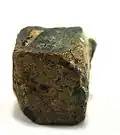 Rutherfordin (gelblichbrauner Belag) auf Uraninit aus dem Ulugurugebirge, Tansania (0,9&nbsp;cm × 0,8&nbsp;cm × 0,7&nbsp;cm)