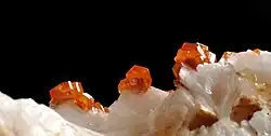 Orangerote Vanadinitkristalle mit dunkelrotem Zentrum auf farblosem Baryt aus Mibladen (Bildbreite ca. 10 mm)