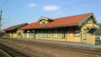 Foto eines hölzernen Bahnhofgebäudes. Im Vordergrund befinden sich Gleise.