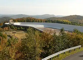 Blick von der Aussichtsplattform Peterskopf am Oberbecken&nbsp;II etwa nach Südosten zum leeren Oberbecken&nbsp;I (mit Einlaufbauwerk; auf dem Peterskopf) der Pumpspeicherwerke Waldeck mit Bergen des Kellerwaldes im Hintergrund