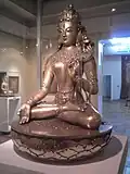 Eine bronzefarbene Figur sitzt im Schneidersitz.
