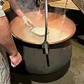Nachdem Essigsäure hinzugefügt wird, flockt der Käse aus und wird mit einer Holzschaufel aus dem Kessel genommen.