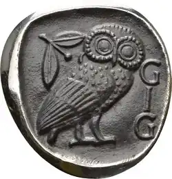 Emblem der GIG auf der Basis einer attischen Tetradrachme (ca. 430 v.&nbsp;Chr.) mit den Initialen der Gesellschaft