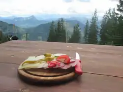 Im Vordergrund ein Brotzeitbrett auf einer Biertischgarnitur, im Hintergrund die Allgäuer und Tannheimer Alpen
