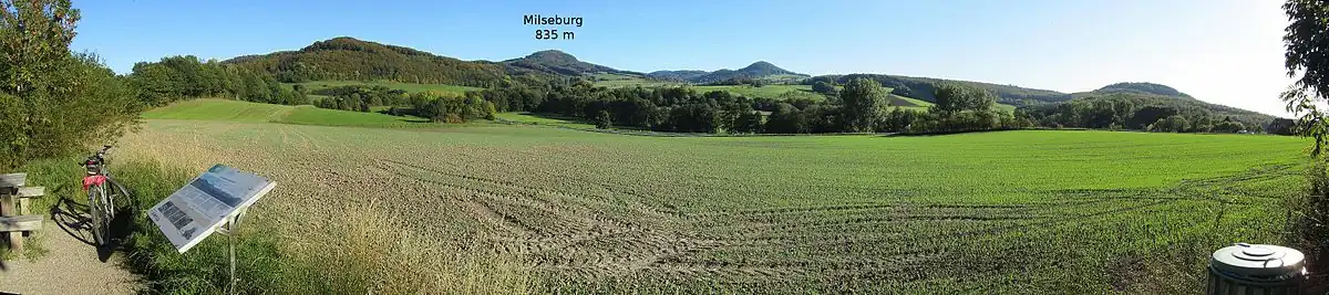 Panorama am Rastplatz in der Schleife (unterhalb des ehemaligen Haltepunktes Biberstein gelegen): Der namensgebende Berg des Weges, die 835 m hohe Milseburg, ist im Bild markiert. Vor Ort steht eine Panoramatafel, die alle Berge im Ausblick vorstellt.