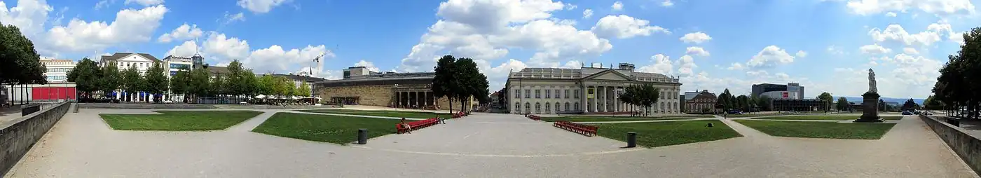 Friedrichsplatz in Kassel: Der weite Platz ist mit die erste Anlaufstelle für Besucher in der Stadtmitte. In der Mitte rechts liegt das historische Gebäude des Fridericianums. Ganz rechts das Denkmal Landgraf Friedrich II. Die roten Bänke in der Bildmitte stammen übrigens von der Documenta 12 aus dem Jahr 2007. Die Bänke besaßen wohl keine tiefer gehende Bedeutung als Kunstwerk (ob sie eventuell in künstlerischem Zusammenhang mit dem ebenfalls roten Mohnfeld der Documenta 12 auf dem Platz standen, ist nicht bekannt). Da die Kasseler sie aber mochten, kaufte die Stadt die markanten Sitzmöbel für insgesamt 8.000 € auf, damit sie dauerhaft Teil der Stadtmöblierung werden konnten.